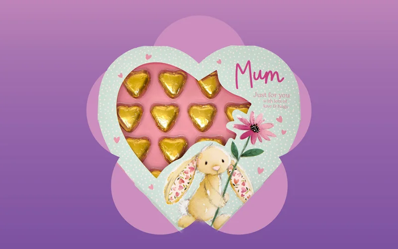 A pink rectangular gift box decorated with hearts and an illustration of a bunny, featuring the text ‘Little treats for lovely you!,’ held in a store aisle against a purple and pink gradient background.