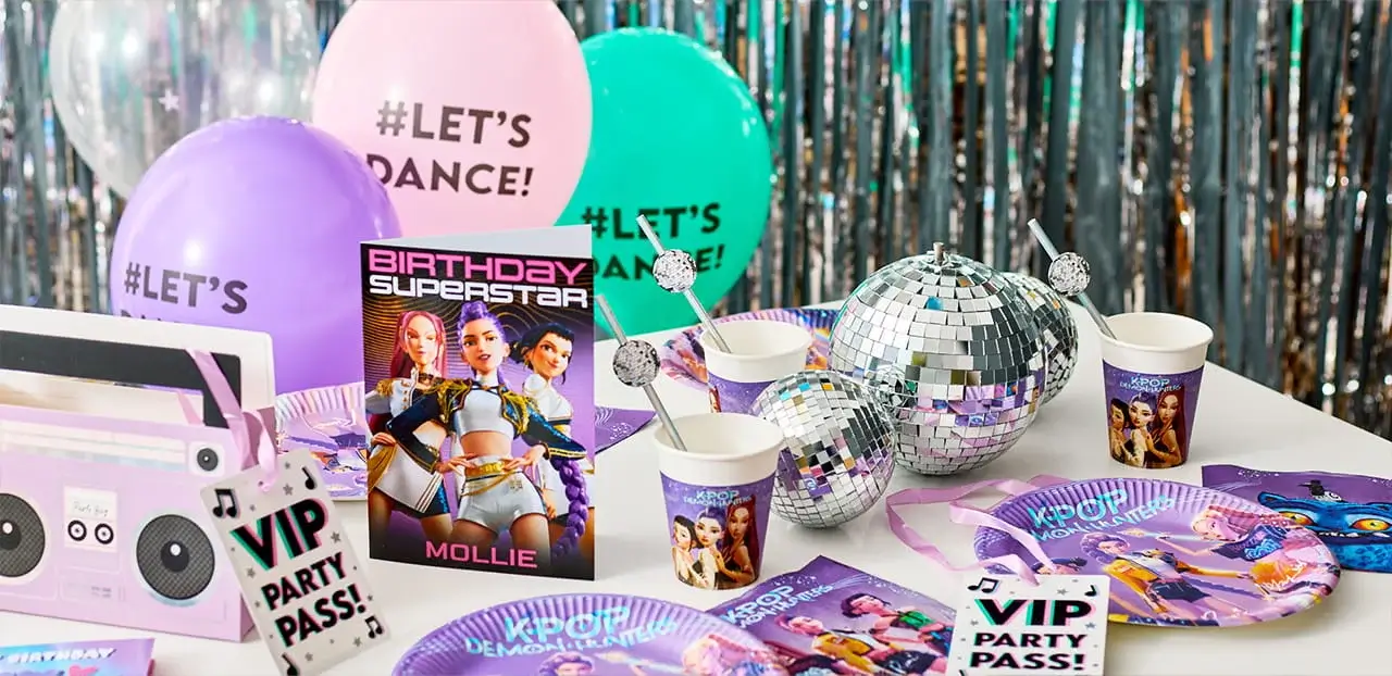 KPop Demon Hunters themed party table with character tableware, disco ball decorations, balloons, VIP party passes, and matching birthday accessories.