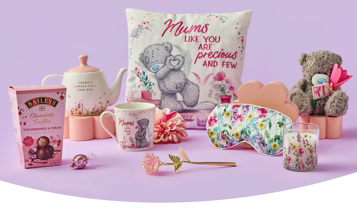 Soft pink Mother’s Day gift display featuring a teddy‑themed cushion, floral teapot, matching mug, Baileys chocolate truffles, a flower eye mask, a scented candle, a plush teddy with a heart, and scattered floral accents. Soft pink Mother’s Day gift display featuring a teddy‑themed cushion, floral teapot, matching mug, Baileys chocolate truffles, a flower eye mask, a scented candle, a plush teddy with a heart, and scattered floral accents.