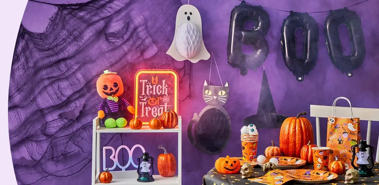Halloween setup with BOO balloons, hanging ghost, black cat cutout, pumpkin decorations, Trick or Treat sign, and festive tableware against a purple backdrop. Halloween setup with BOO balloons, hanging ghost, black cat cutout, pumpkin decorations, Trick or Treat sign, and festive tableware against a purple backdrop.