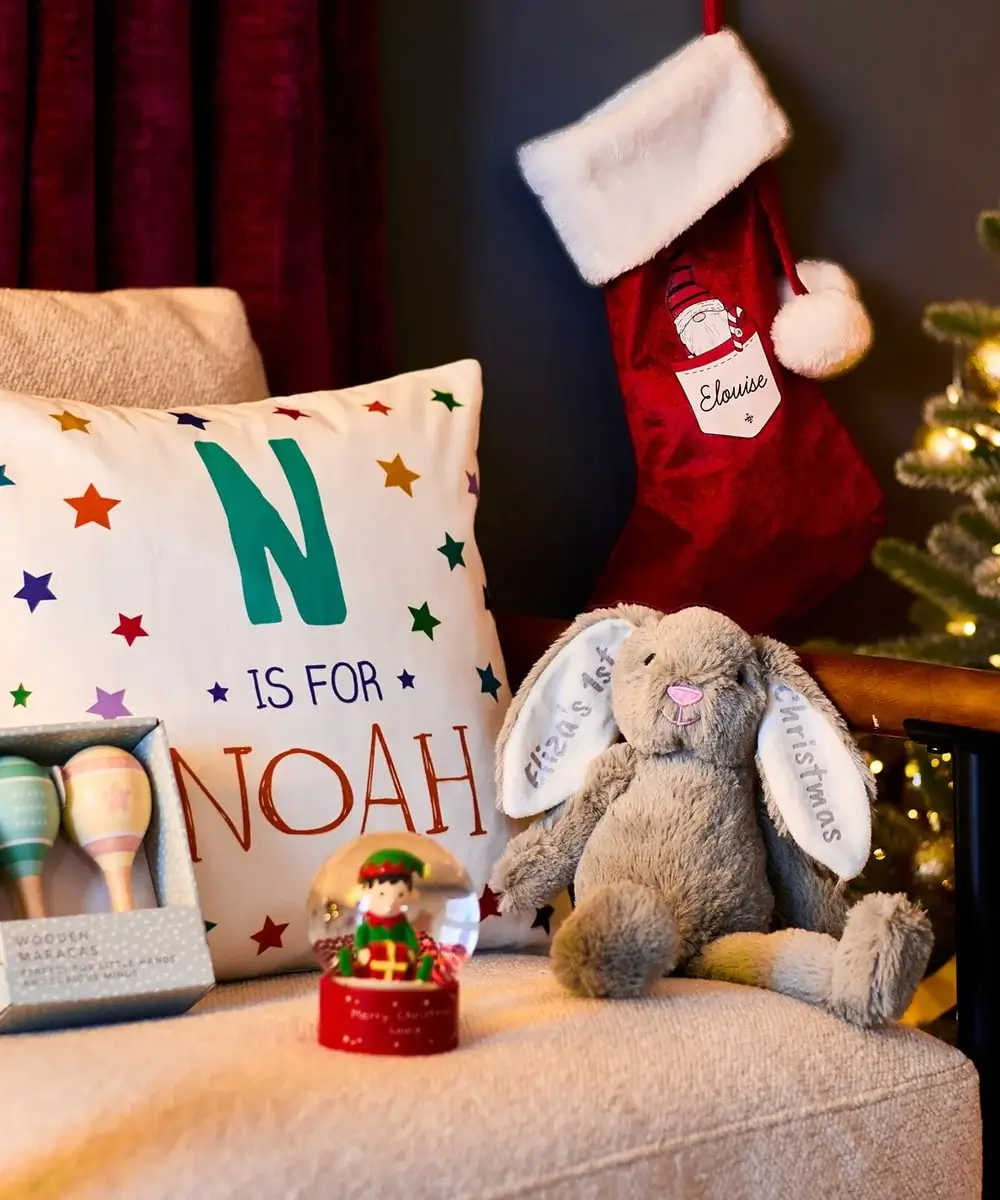 Cozy Christmas scene with a personalized Noah pillow, Eloise stocking, plush bunny with First Christmas embroidery, elf snow globe, and pastel wooden maracas in a box. Cozy Christmas scene with a personalized Noah pillow, Eloise stocking, plush bunny with First Christmas embroidery, elf snow globe, and pastel wooden maracas in a box.