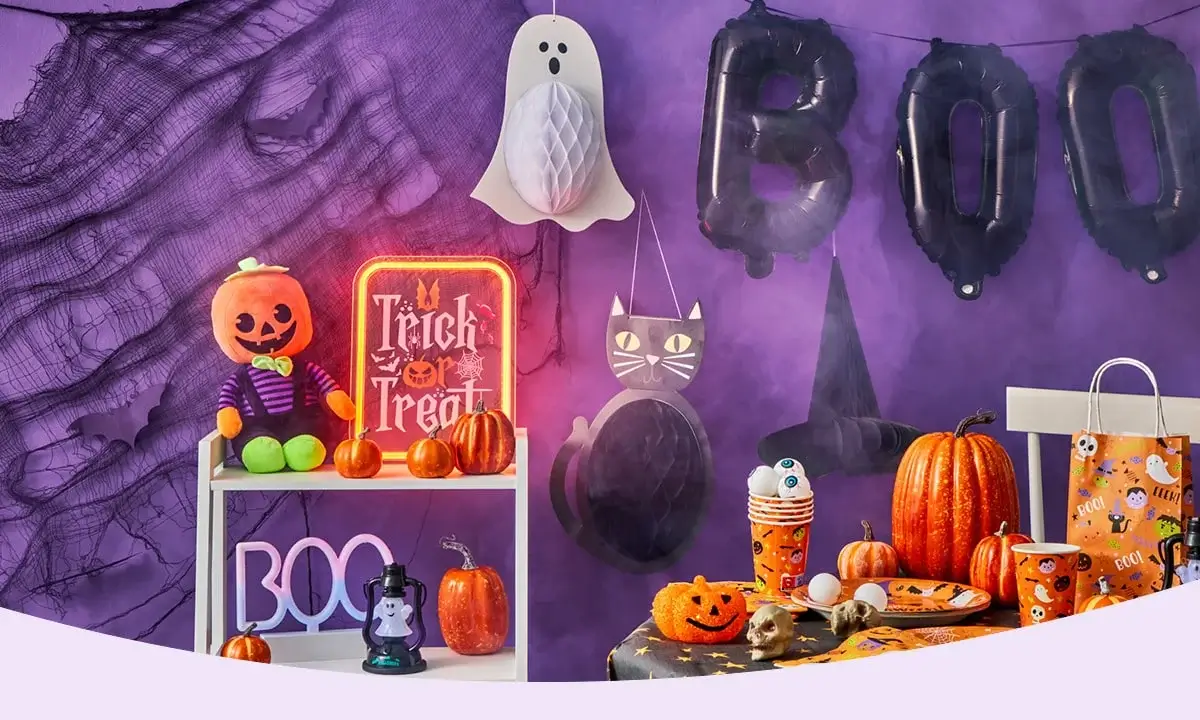 Halloween setup with BOO balloons, hanging ghost, black cat cutout, pumpkin decorations, Trick or Treat sign, and festive tableware against a purple backdrop. Halloween setup with BOO balloons, hanging ghost, black cat cutout, pumpkin decorations, Trick or Treat sign, and festive tableware against a purple backdrop.