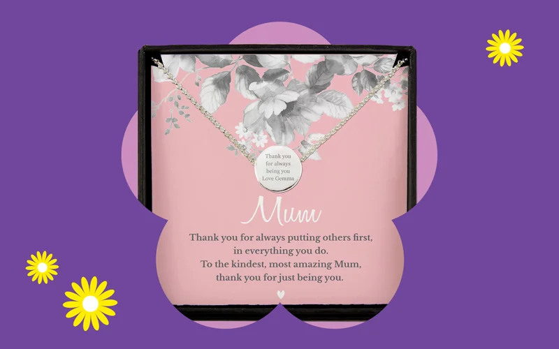 A necklace presented in a gift box with floral designs and a pink background, featuring a round pendant with a thank‑you message for Mum.”