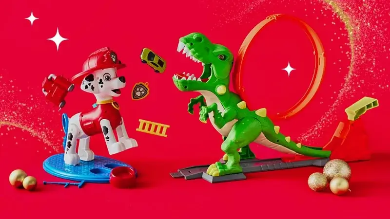 Toy Dalmatian firefighter and green dinosaur on a red background with a loop track, flying toy cars, firefighting accessories, and gold Christmas ornaments. Toy Dalmatian firefighter and green dinosaur on a red background with a loop track, flying toy cars, firefighting accessories, and gold Christmas ornaments.