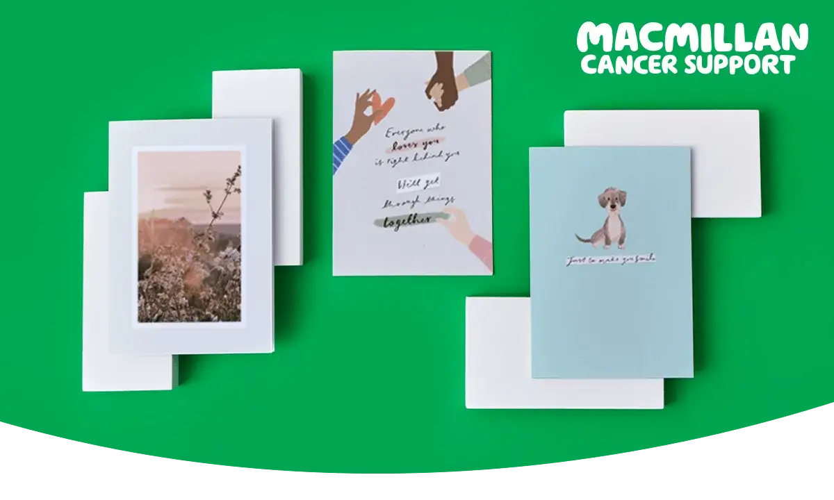 Three greeting cards displayed on a bright green background with white envelopes. The left card features a scenic photograph of flowers and hills, the center card shows illustrated hands holding each other with text that reads “Everyone who knows you is right behind you. We’ll get through things together,” and the right card has a simple design with a cute dog illustration and text that says “Just to make you smile.” The Macmillan Cancer Support logo appears in the top right corner.