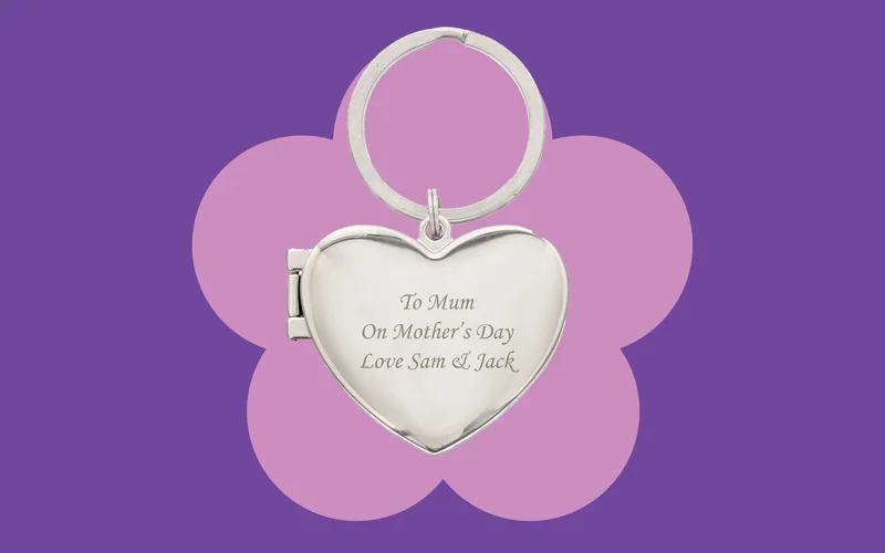 A silver heart‑shaped keyring with an engraved message reading ‘To Mum, On Mother’s Day, Love Sam & Jack,’ displayed against a purple background with a pink flower shape.