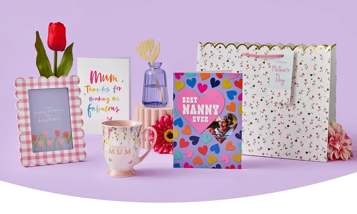 A colourful Mother’s Day display featuring greeting cards, a red tulip, a blue reed diffuser bottle, a floral Mum mug, a pink gingham photo frame, and a patterned gift bag arranged with bright flowers on a lilac background. A colourful Mother’s Day display featuring greeting cards, a red tulip, a blue reed diffuser bottle, a floral Mum mug, a pink gingham photo frame, and a patterned gift bag arranged with bright flowers on a lilac background.