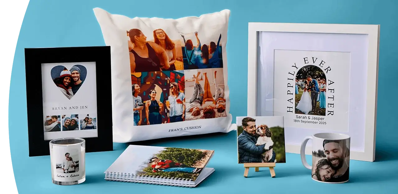 A display of personalised photo gifts including a framed print, a collage cushion, a wedding-themed wall print, a photo candle, a photo notebook, a small photo canvas on a stand and a photo mug arranged against a blue background. A display of personalised photo gifts including a framed print, a collage cushion, a wedding-themed wall print, a photo candle, a photo notebook, a small photo canvas on a stand and a photo mug arranged against a blue background.