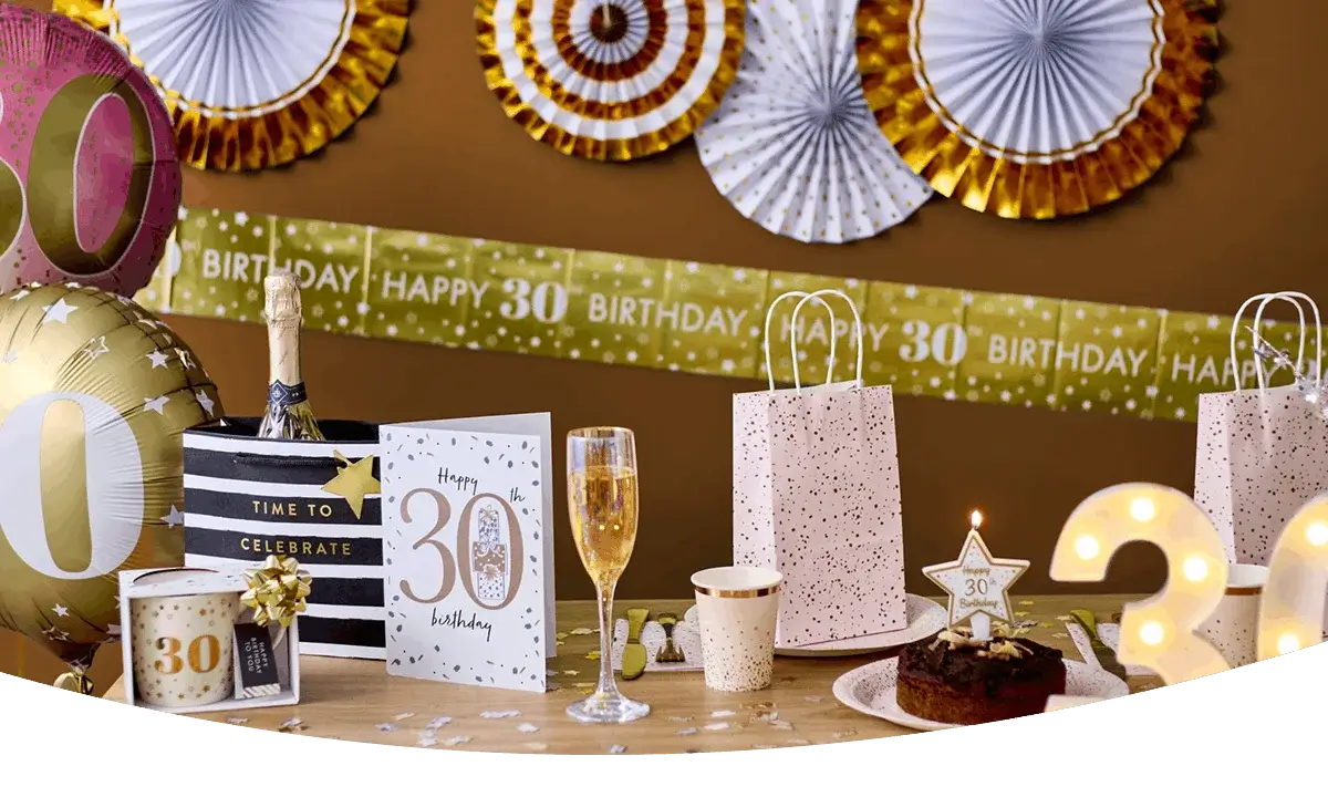 30th birthday celebration table with balloons, a birthday banner, champagne glass, gift bags, birthday cake, and gold party decorations. 30th birthday celebration table with balloons, a birthday banner, champagne glass, gift bags, birthday cake, and gold party decorations.