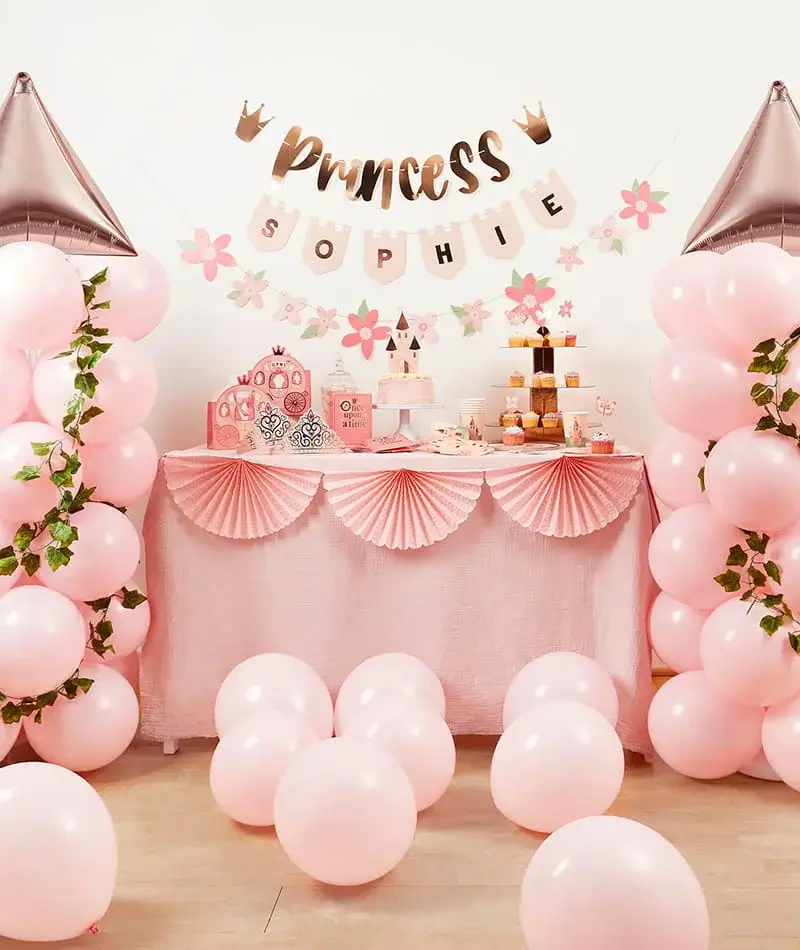 Princess-themed party setup with pink balloons, personalised banner, floral decorations, cupcakes, and matching tableware on display. Princess-themed party setup with pink balloons, personalised banner, floral decorations, cupcakes, and matching tableware on display.