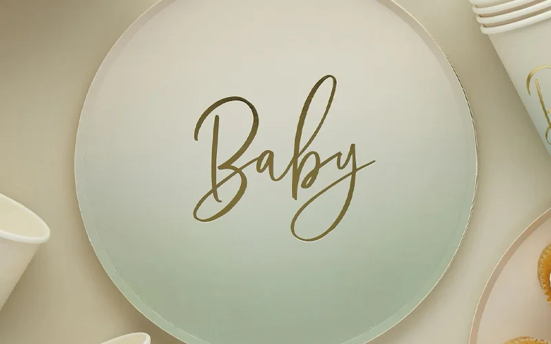 A round white baby shower plate with elegant gold script lettering reading ‘Baby,’ displayed as part of a coordinated neutral-toned baby shower tableware collection.