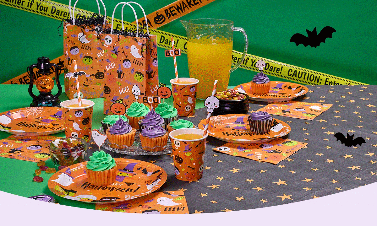 Halloween party setup with orange and black decorations, ghost and pumpkin-themed tableware, cupcakes with green and purple frosting, a pitcher of orange juice, black lantern, candy bowl, and yellow caution tape reading Enter if You Dare across a green backdrop with bat cutouts.