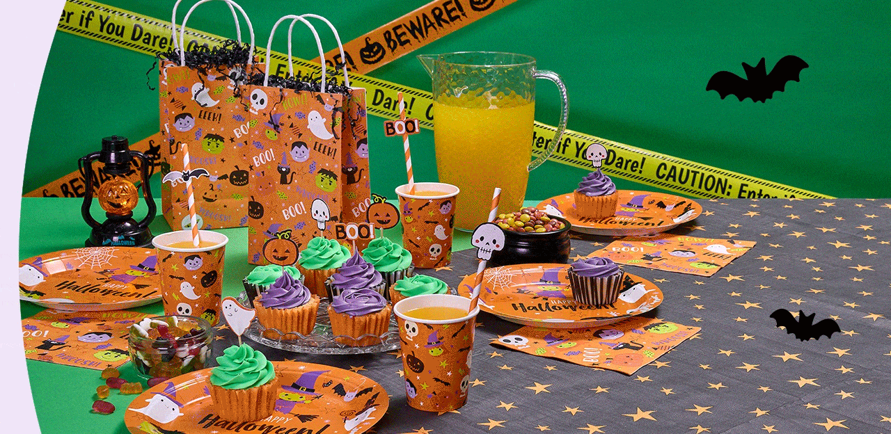 Halloween party setup with orange and black decorations, ghost and pumpkin-themed tableware, cupcakes with green and purple frosting, a pitcher of orange juice, black lantern, candy bowl, and yellow caution tape reading Enter if You Dare across a green backdrop with bat cutouts.