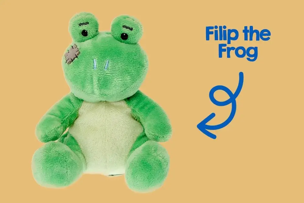 A green plush frog toy with a light beige belly and limbs, sitting against a pink background. The frog has two black eyes, stitched eyebrows, and a patch on its left cheek. A green plush frog toy with a light beige belly and limbs, sitting against a pink background. The frog has two black eyes, stitched eyebrows, and a patch on its left cheek.