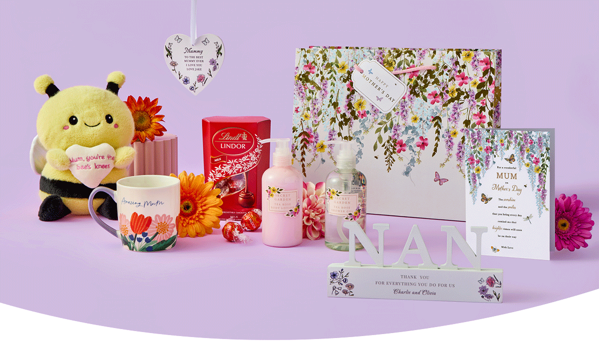 Floral‑themed Mother’s Day gift set featuring a plush bee holding a heart, a flower mug, chocolates, lotion, a decorative heart plaque, a patterned gift box, a framed card, and a NAN ornament arranged on a pastel purple background.