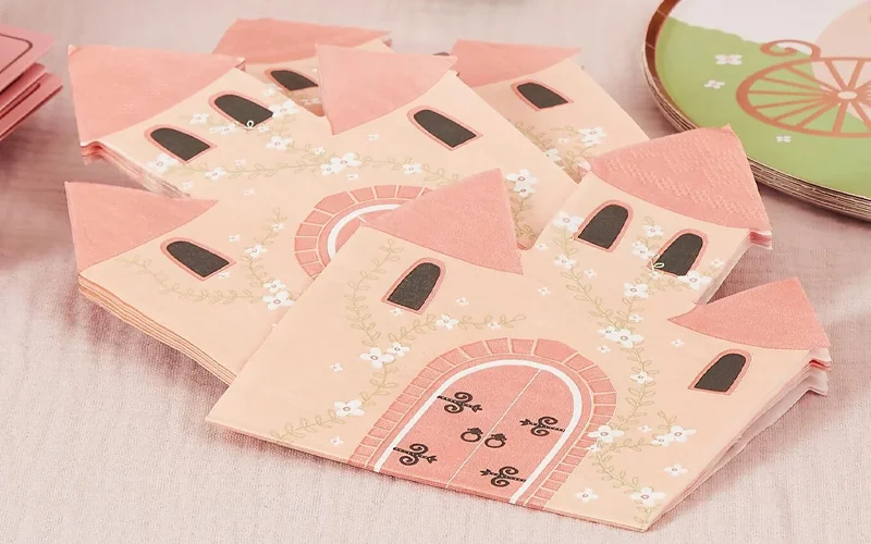 A stack of princess-themed paper napkins shaped like a fairytale castle, featuring pastel pink towers, arched doors, floral details and glitter-effect accents, displayed on a soft pink table covering. A stack of princess-themed paper napkins shaped like a fairytale castle, featuring pastel pink towers, arched doors, floral details and glitter-effect accents, displayed on a soft pink table covering.