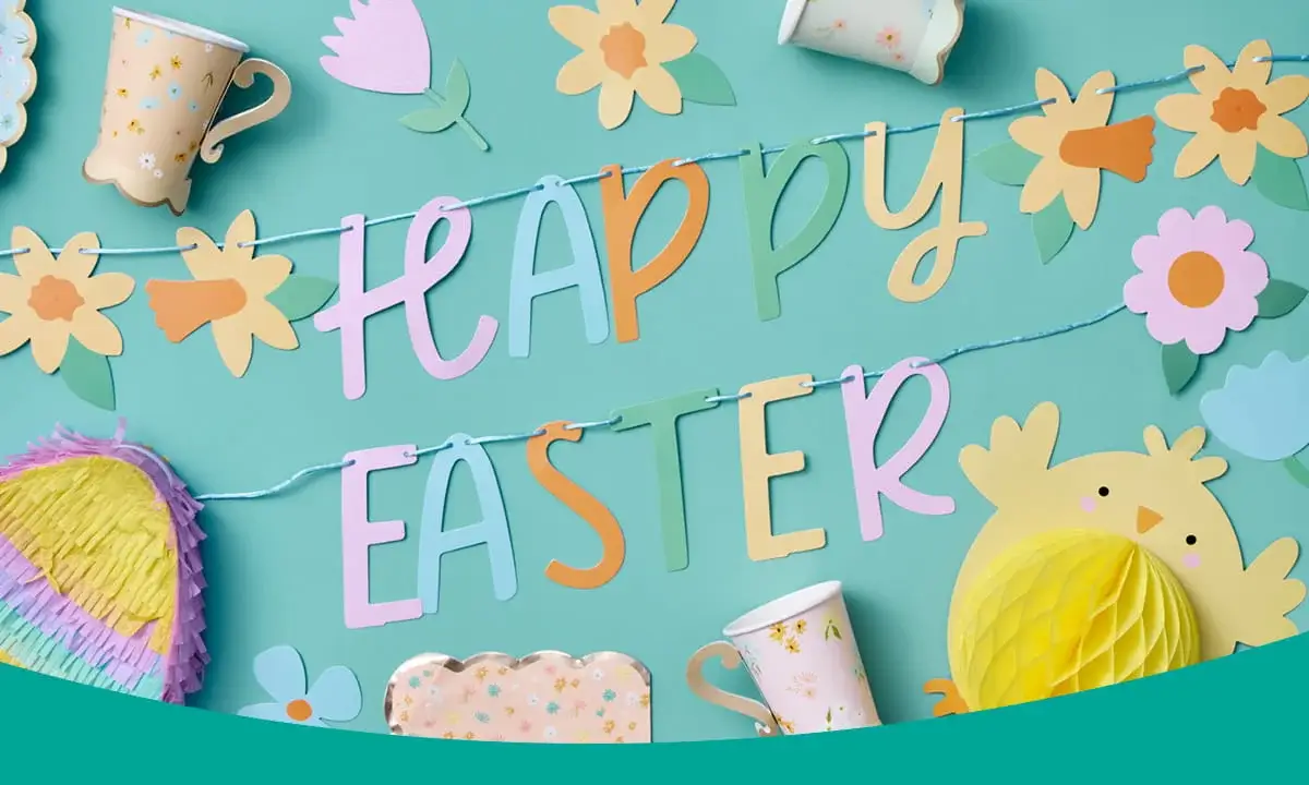 Colourful Easter decorations arranged on a teal background, featuring a Happy Easter banner, floral cut-outs, paper cups and a yellow chick decoration.