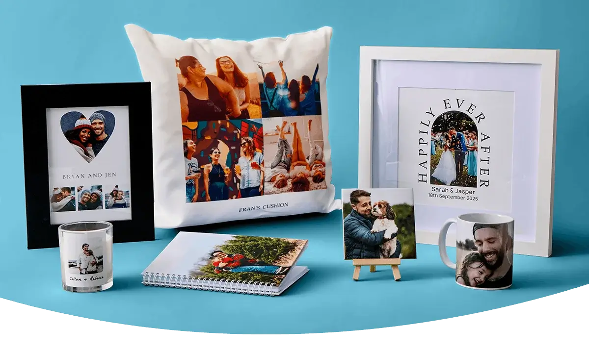 A display of personalised photo gifts including a framed print, a collage cushion, a wedding-themed wall print, a photo candle, a photo notebook, a small photo canvas on a stand and a photo mug arranged against a blue background. A display of personalised photo gifts including a framed print, a collage cushion, a wedding-themed wall print, a photo candle, a photo notebook, a small photo canvas on a stand and a photo mug arranged against a blue background.
