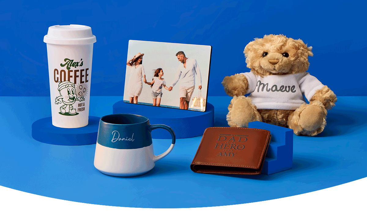 A cosy home display featuring personalised wall art, a wooden clock, a table lamp, framed prints, decorative accessories and a cushion with a highland cow design arranged against a dark blue wall.