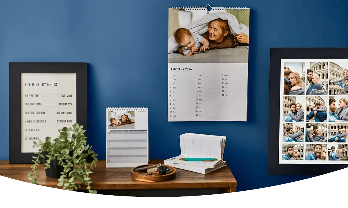 Personalised photo calendars and framed photo prints displayed on a wooden shelf against a blue wall, featuring family and travel photographs. Personalised photo calendars and framed photo prints displayed on a wooden shelf against a blue wall, featuring family and travel photographs.