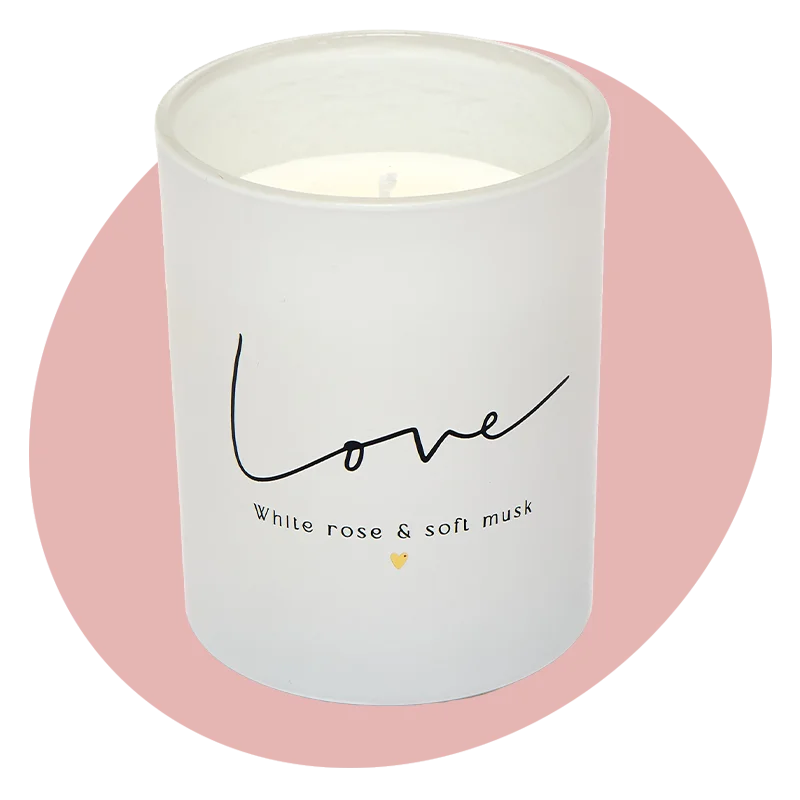 A white glass candle labelled ‘Love – white rose & soft musk’ with a small gold heart detail, displayed against a soft pink circular background. AA white glass candle labelled ‘Love – white rose & soft musk’ with a small gold heart detail, displayed against a soft pink circular background.