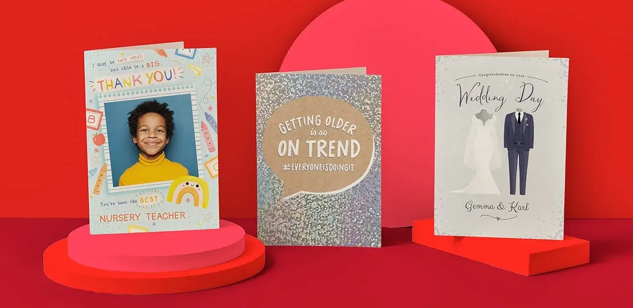 Three greeting cards are displayed on a blue background. The first is a thank you card for a nursery teacher with a photo of a person whose face is obscured. The middle card reads 'Getting older is so on trend #everyoneisdoingit' with a glittery design. The third is a wedding day card with an illustration of a wedding dress and suit, addressed to Gemma & Karl.