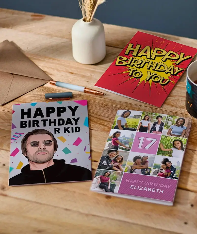 Selection of birthday cards including personalised photo cards, a character-themed card, and a humorous birthday card displayed on a wooden table.
