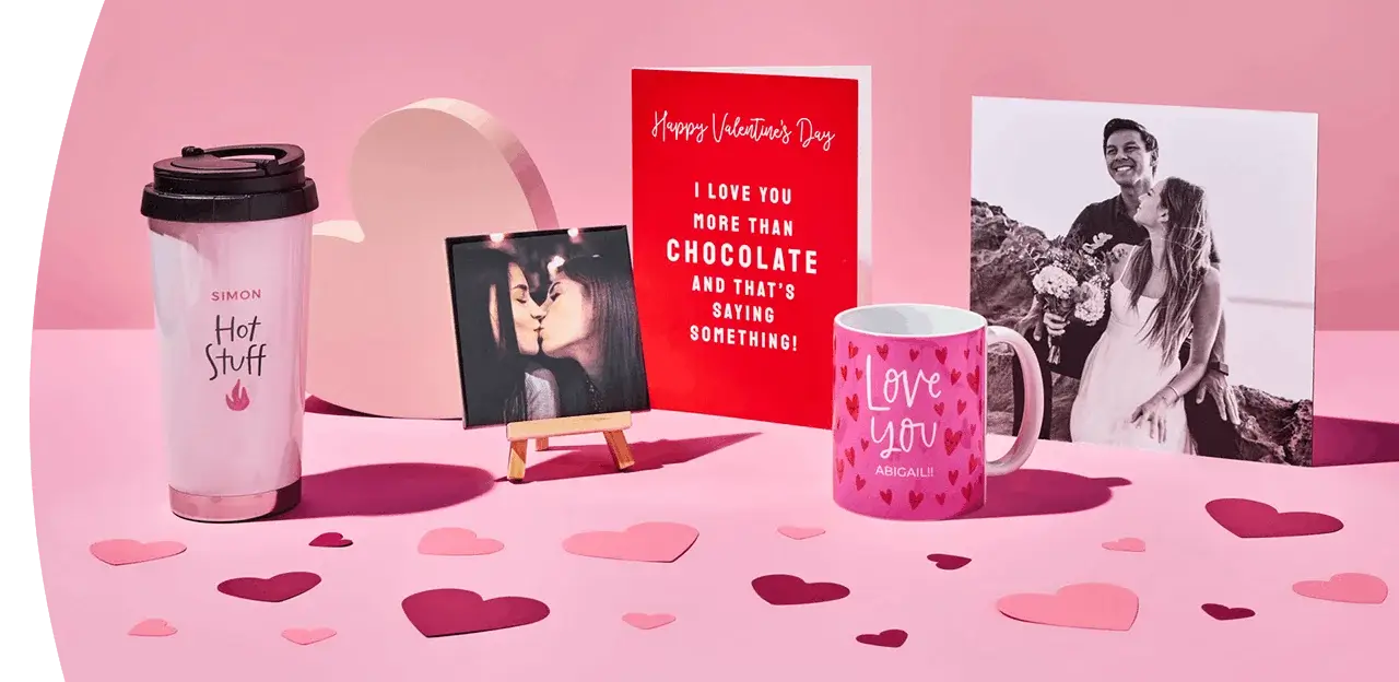 A Valentine’s display featuring a personalised travel cup, a framed photo, a bright red greeting card, a pink love‑themed mug, and a large romantic photo print, arranged on a pink surface with scattered heart cutouts. A Valentine’s display featuring a personalised travel cup, a framed photo, a bright red greeting card, a pink love‑themed mug, and a large romantic photo print, arranged on a pink surface with scattered heart cutouts.
