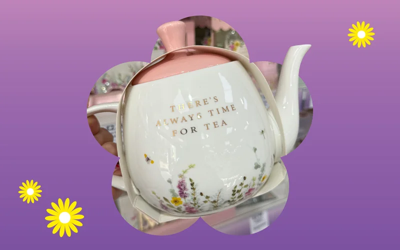 A ceramic teapot with a pink lid and floral illustrations, featuring the phrase ‘There’s always time for tea,’ displayed against a purple and pink gradient background with small yellow daisies.