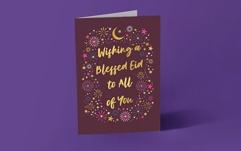 AA maroon Eid greeting card decorated with gold and pink stars, fireworks and a crescent moon, featuring the message ‘Wishing a Blessed Eid to All of You.
