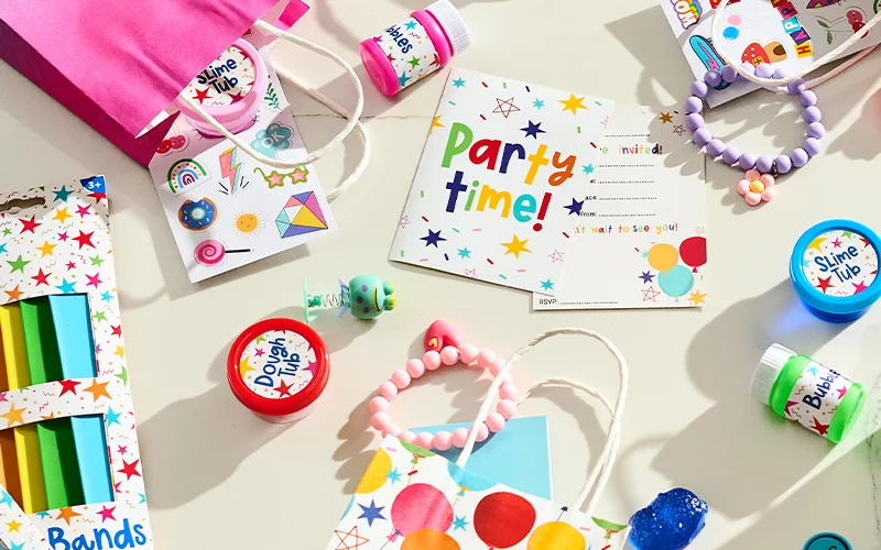 A flat-lay display of children's party bag fillers and party accessories, including a ‘Party Time!’ invitation, colourful gift bags, sticker sheets, bead bracelets, tubs of slime and dough, bubbles, crayons, novelty toys and small party favours arranged on a light background. A flat-lay display of children's party bag fillers and party accessories, including a ‘Party Time!’ invitation, colourful gift bags, sticker sheets, bead bracelets, tubs of slime and dough, bubbles, crayons, novelty toys and small party favours arranged on a light background.
