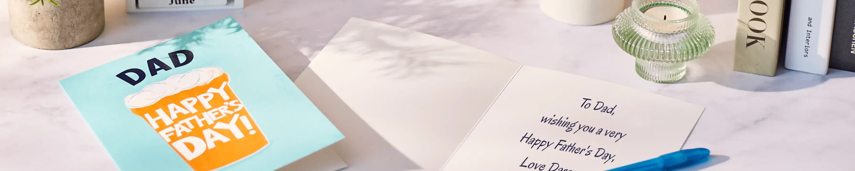 An open Father’s Day card on a light tabletop, showing a turquoise front with a beer illustration and the text ‘Dad Happy Father’s Day,’ alongside the inside message reading ‘To Dad, wishing you a very happy Father’s Day,’ with a pen, candle and books nearby. An open Father’s Day card on a light tabletop, showing a turquoise front with a beer illustration and the text ‘Dad Happy Father’s Day,’ alongside the inside message reading ‘To Dad, wishing you a very happy Father’s Day,’ with a pen, candle and books nearby.