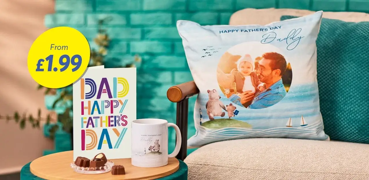 'A Father's Day gift display featuring a colorful card that reads 'DAD HAPPY FATHER'S DAY', a white mug with an illustration of two bears and the text 'HAPPY FATHER'S DAY', and a decorative pillow with an image of a father holding a baby, accompanied by the text 'HAPPY FATHER'S DAY Daddy'. The display also includes chocolates on a small plate, all set against a teal background. A yellow circular label in the top left corner states 'From £1.99'.