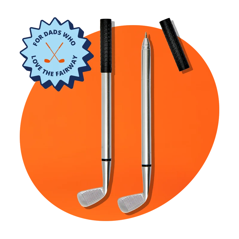 A novelty pen set designed to look like two silver golf clubs with black grip handles, displayed against a bright orange background with a blue badge reading ‘For dads who love the fairway. A novelty pen set designed to look like two silver golf clubs with black grip handles, displayed against a bright orange background with a blue badge reading ‘For dads who love the fairway.