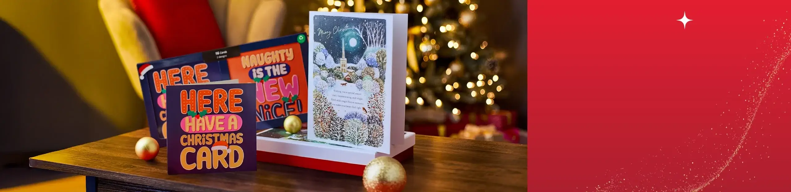 Festive scene with three Christmas cards on a wooden table alongside two gold ornaments, featuring bold and playful designs with messages HERE HAVE A CHRISTMAS CARD, NAUGHTY IS THE NEW NICE, and Merry Christmas, set against a blurred background of a decorated Christmas tree. Festive scene with three Christmas cards on a wooden table alongside two gold ornaments, featuring bold and playful designs with messages HERE HAVE A CHRISTMAS CARD, NAUGHTY IS THE NEW NICE, and Merry Christmas, set against a blurred background of a decorated Christmas tree.