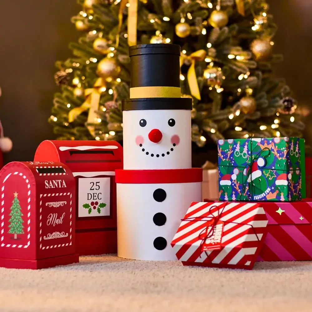 Christmas gift boxes and a snowman-shaped container placed in front of a decorated Christmas tree with golden ornaments and lights.