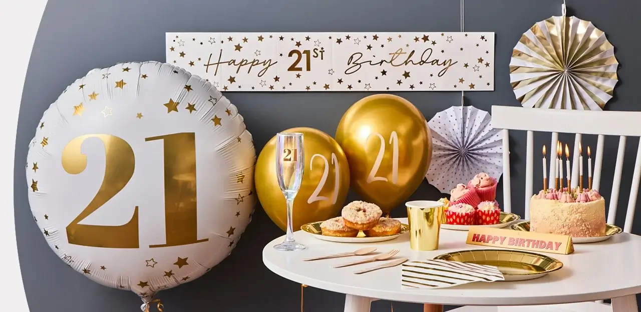 T21st birthday setup with gold balloons, champagne flute, cake, cupcakes, donuts, and a Happy 21st Birthday banner.
