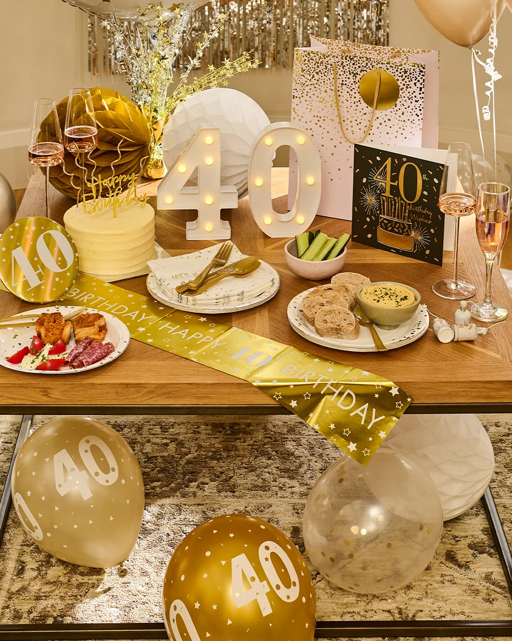A gold, white and black 40th birthday tablescape featuring illuminated number 40 lights, a birthday cake with a ‘Happy Birthday’ topper, champagne flutes, gold-accented tableware, a ‘40th Birthday Wishes’ card, gift bags and milestone birthday balloons. Gold and white decorations, confetti balloons and a ‘Happy 40th Birthday’ table runner complete the elegant celebration display. A gold, white and black 40th birthday tablescape featuring illuminated number 40 lights, a birthday cake with a ‘Happy Birthday’ topper, champagne flutes, gold-accented tableware, a ‘40th Birthday Wishes’ card, gift bags and milestone birthday balloons. Gold and white decorations, confetti balloons and a ‘Happy 40th Birthday’ table runner complete the elegant celebration display.