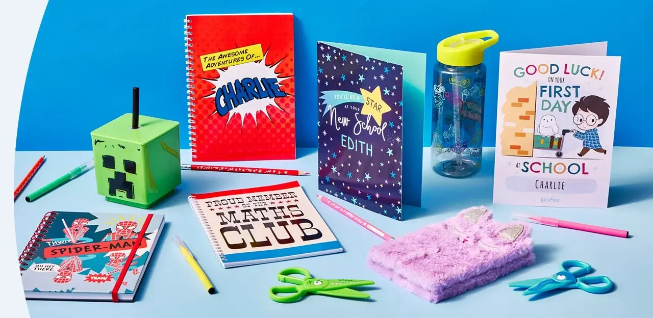 Assorted school supplies and personalised items on a blue surface, including notebooks, pencils, a Minecraft pencil holder, and greeting cards for Edith and Charlie.