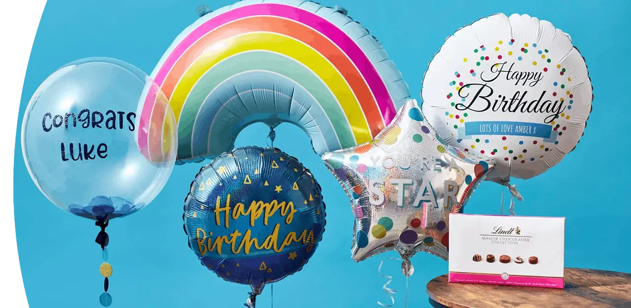 Balloon display featuring a rainbow balloon, birthday balloons, a Congrats Luke balloon, and a box of chocolates arranged against a bright blue background.