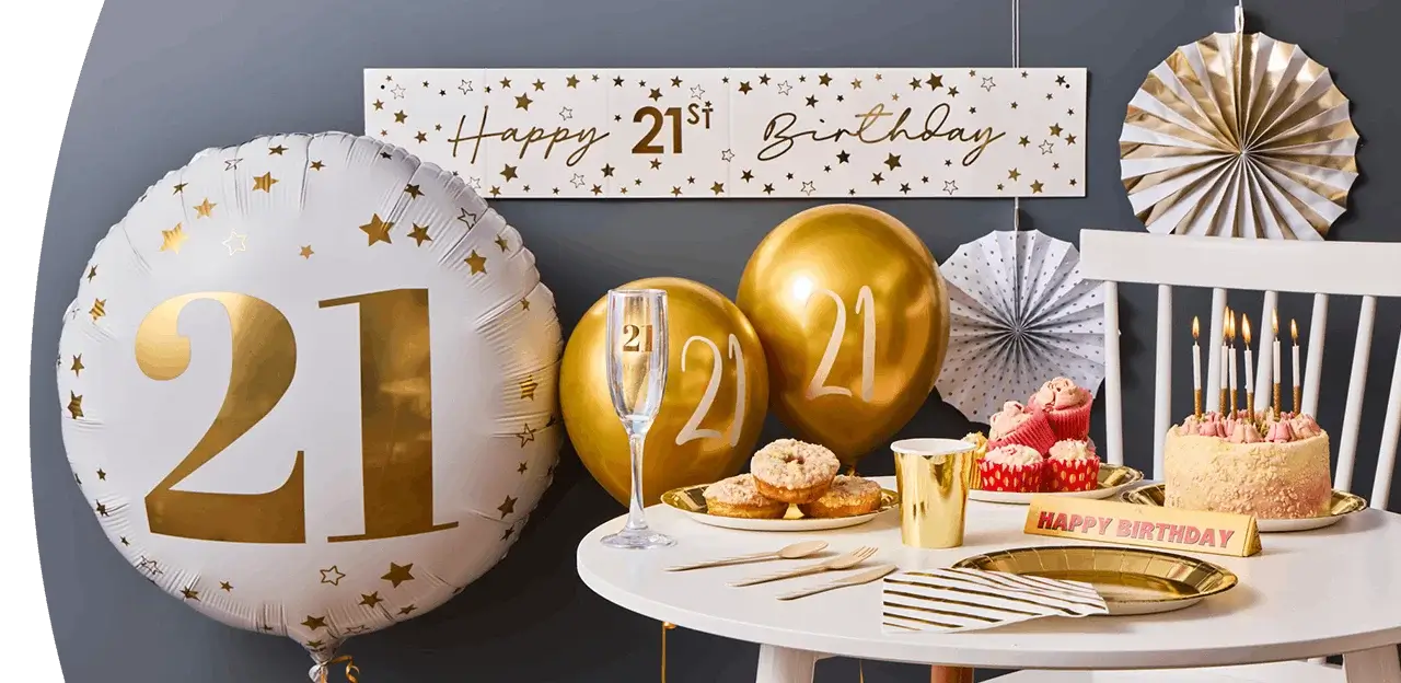 Gold and white 21st birthday setup with large balloons, a decorated cake with candles, cupcakes, party tableware, and a festive banner. Gold and white 21st birthday setup with large balloons, a decorated cake with candles, cupcakes, party tableware, and a festive banner.