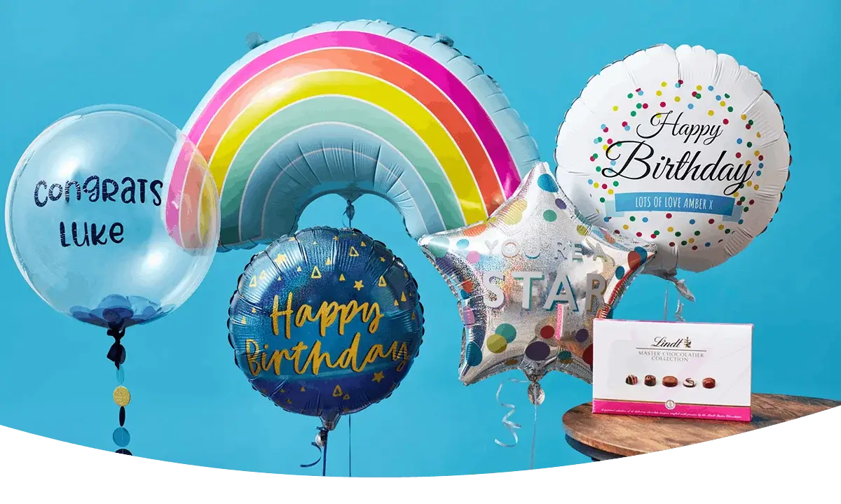 Balloon display featuring a rainbow balloon, birthday balloons, a Congrats Luke balloon, and a box of chocolates arranged against a bright blue background.