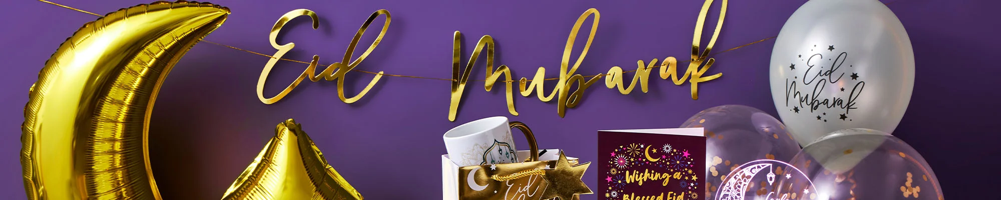 An Eid display featuring gold crescent‑moon and star balloons, a gold ‘Eid Mubarak’ banner, and festive items including a gift bag, mug, greeting cards, transparent balloons with gold confetti, and a lit candle arranged against a purple background.
