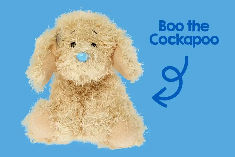 A fluffy, light brown stuffed animal resembling a dog with long ears and a blue nose, sitting against a pink background. A fluffy, light brown stuffed animal resembling a dog with long ears and a blue nose, sitting against a pink background.