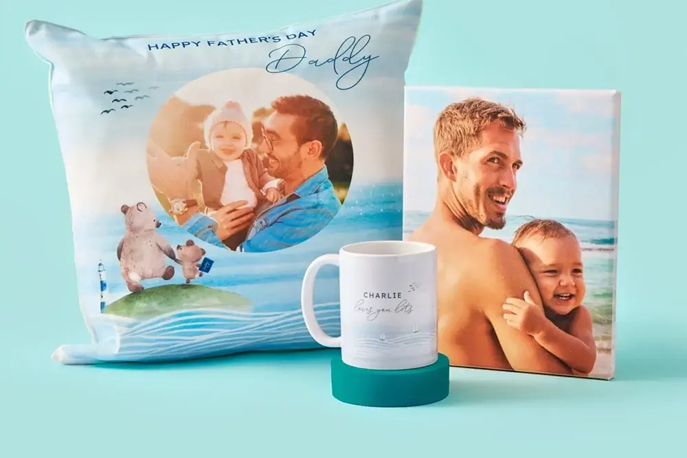 The image shows a personalised gift set for Father's Day, including a pillow, a mug, and a canvas print. The pillow features the text 'HAPPY FATHER'S DAY Daddy' with an image of two people and some illustrated bears. The mug has the text 'CHARLIE loves you lots' with small hearts. The canvas print displays an image of two people embracing. The image shows a personalised gift set for Father's Day, including a pillow, a mug, and a canvas print. The pillow features the text 'HAPPY FATHER'S DAY Daddy' with an image of two people and some illustrated bears. The mug has the text 'CHARLIE loves you lots' with small hearts. The canvas print displays an image of two people embracing.