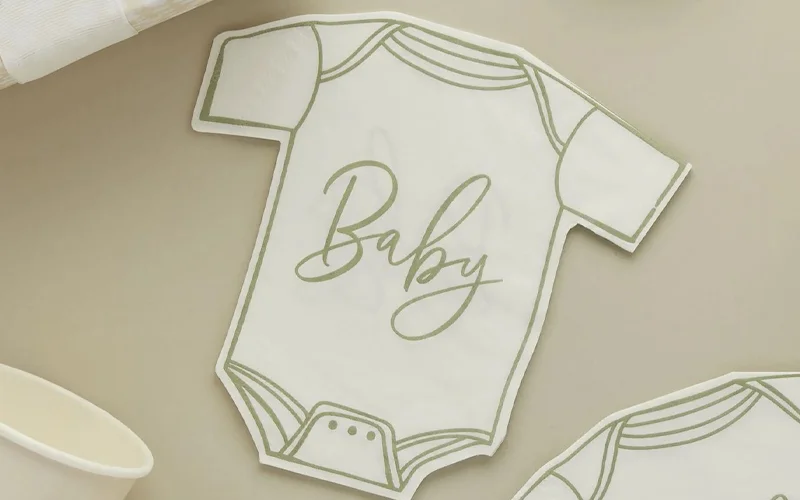 Baby shower napkins shaped like a baby bodysuit, decorated with a sage green outline and gold script lettering reading ‘Baby,’ displayed on a neutral-toned table setting.