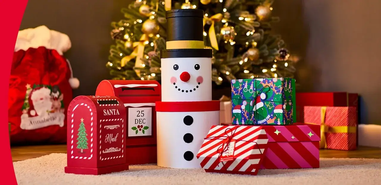 Christmas-themed display with a snowman-shaped gift box, red Santa Mail boxes, and wrapped presents in front of a decorated tree.