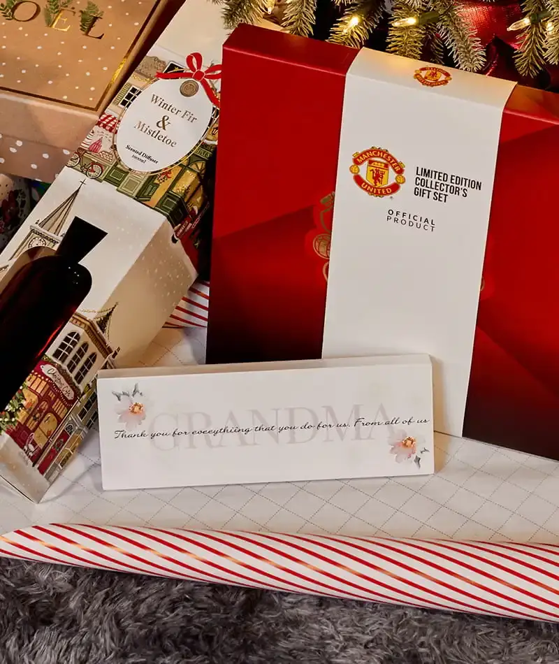 Selection of Christmas gifts, including fragrance sets, a Manchester United collector’s gift set and a sentimental plaque, displayed among wrapped presents beneath a Christmas tree.