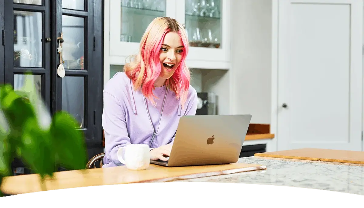 A person sitting at a kitchen table using a laptop, with a mug nearby, in a bright modern home setting.