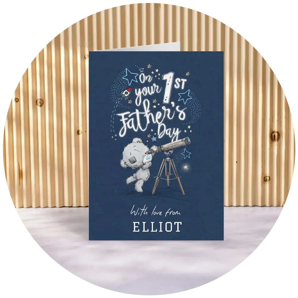 A navy blue first Father’s Day card featuring a Tatty Teddy illustration looking through a telescope, star details, and the text ‘On your 1st Father’s Day,’ with a personalised name printed at the bottom, displayed against a wooden slatted backdrop. A navy blue first Father’s Day card featuring a Tatty Teddy illustration looking through a telescope, star details, and the text ‘On your 1st Father’s Day,’ with a personalised name printed at the bottom, displayed against a wooden slatted backdrop.
